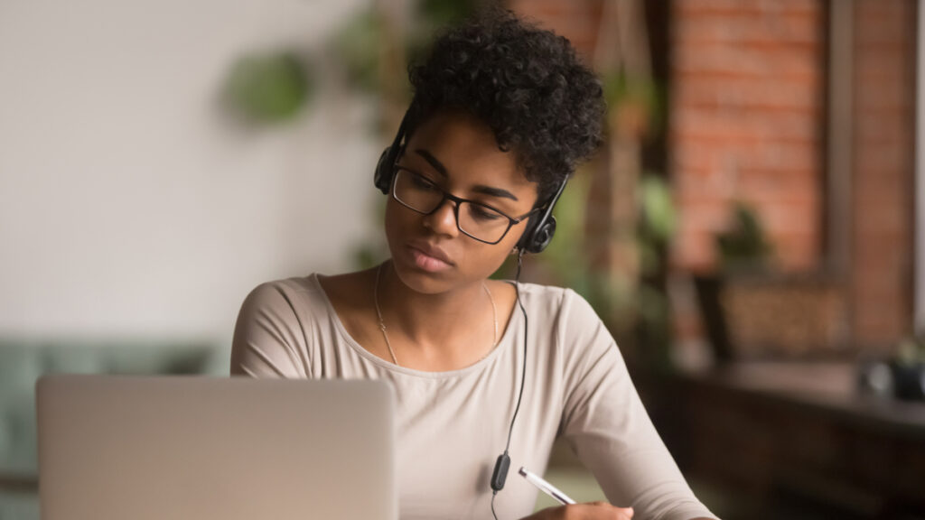 young woman in front of laptop taking notes during an online learning session
